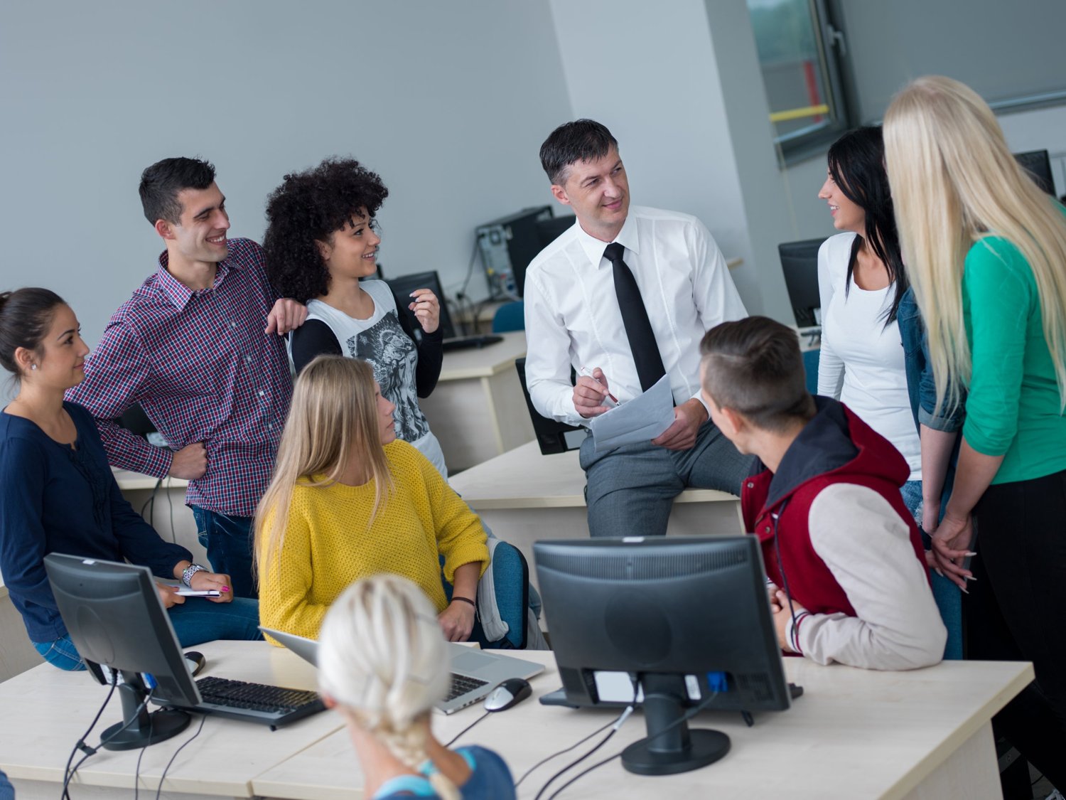 A trainer talking with a group of learners in a computer classroom