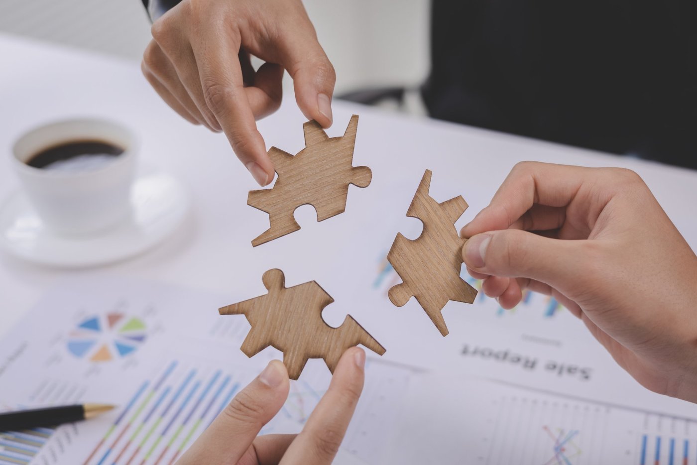 Three hands bringing wooden puzzle pieces together over business reports